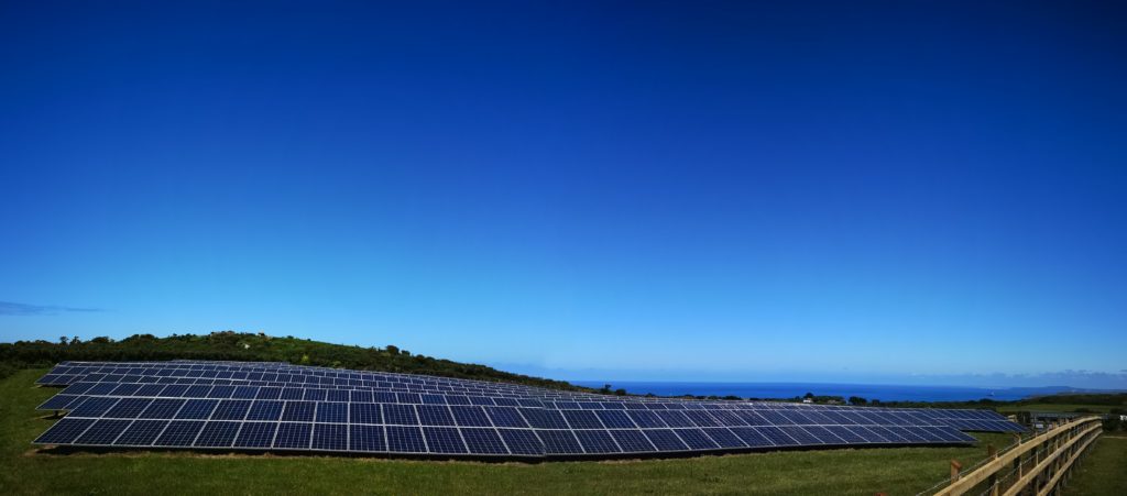 Field of solar panels, with the sea in the distance and bright blue skies