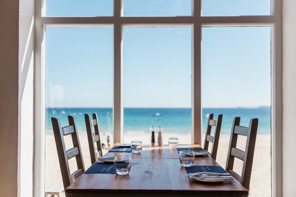 4 seater table situated directly in front of large window looking over the beach and sea.