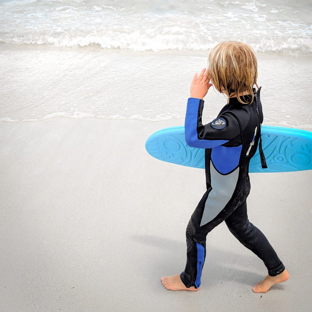 Young child wearing a wetsuit and holding a surfboard on a rainy day in Cornwall