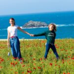 Sisters holding hands in poppy field overlooking the sea as part of a family photo shoot in st ives