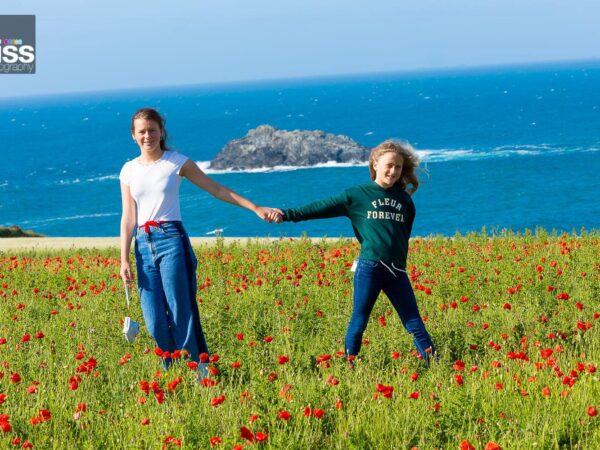 Sisters holding hands in poppy field overlooking the sea as part of a family photo shoot in st ives