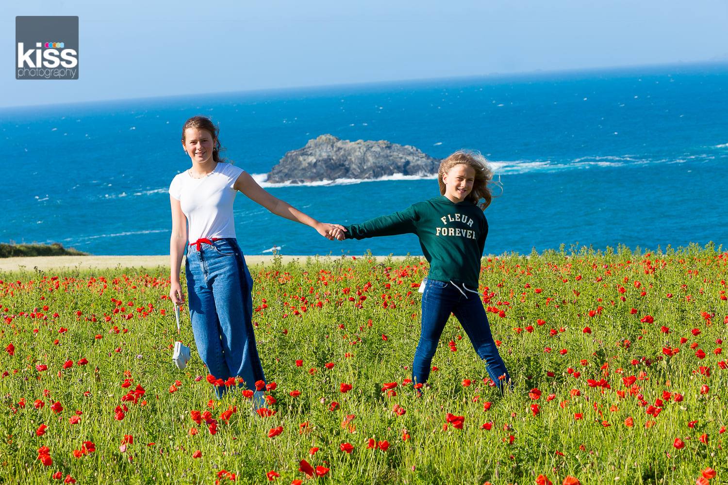 Sisters holding hands in poppy field overlooking the sea as part of a family photo shoot in st ives