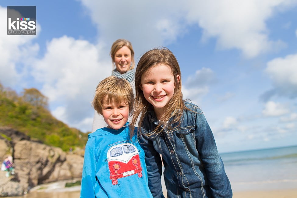 Brother and sister huddled close and smiling with their mum in the background for a family photo shoot in st ives