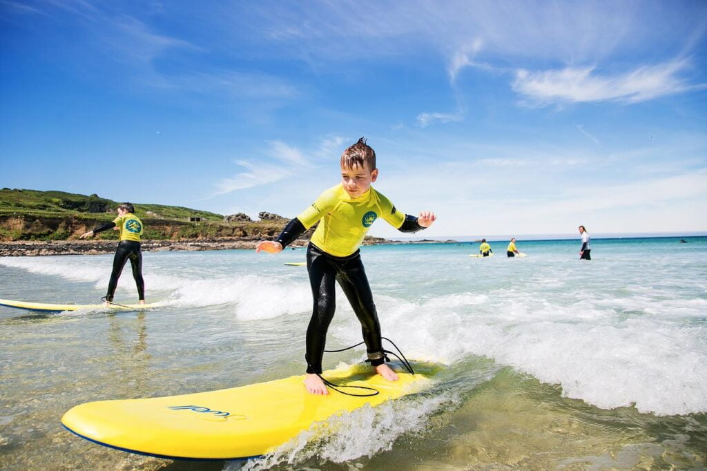 Young boy standing on a surfboard in the sea learning to surf with St Ives Surf School in West Cornwall