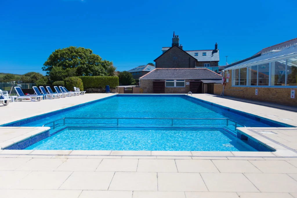 View of Polmanters swimming pool from the shallow end with sun loungers and bright blue sky