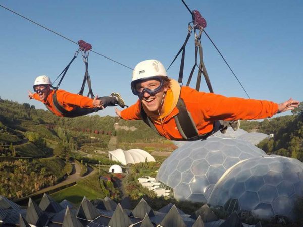 Two smiling people flying high above the Eden biomes on a zipwire